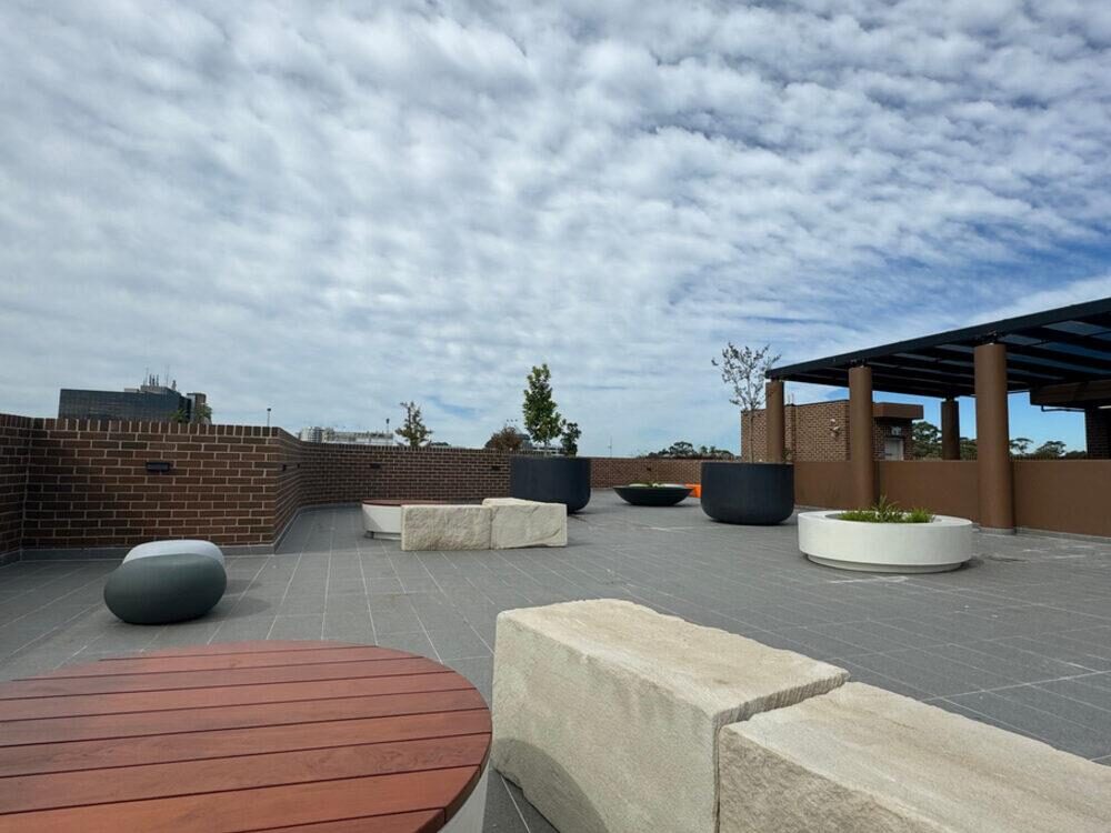 The rooftop garden at the Blacktown apartments, with stone bench seating, a timber deck, planters and a shaded pergola