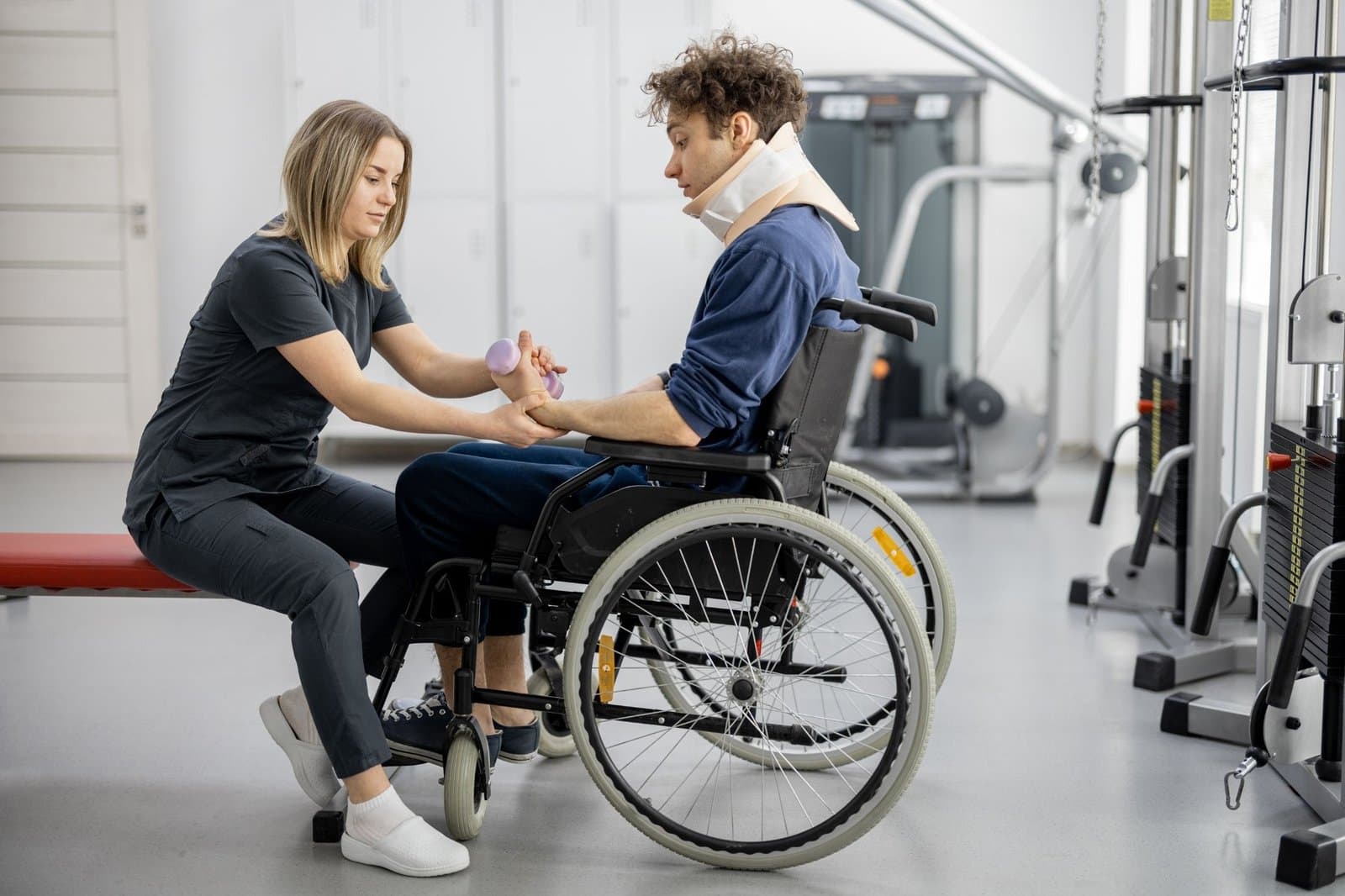 A skilled support worker guiding a young man in a wheelchair through a rehabilitation exercise